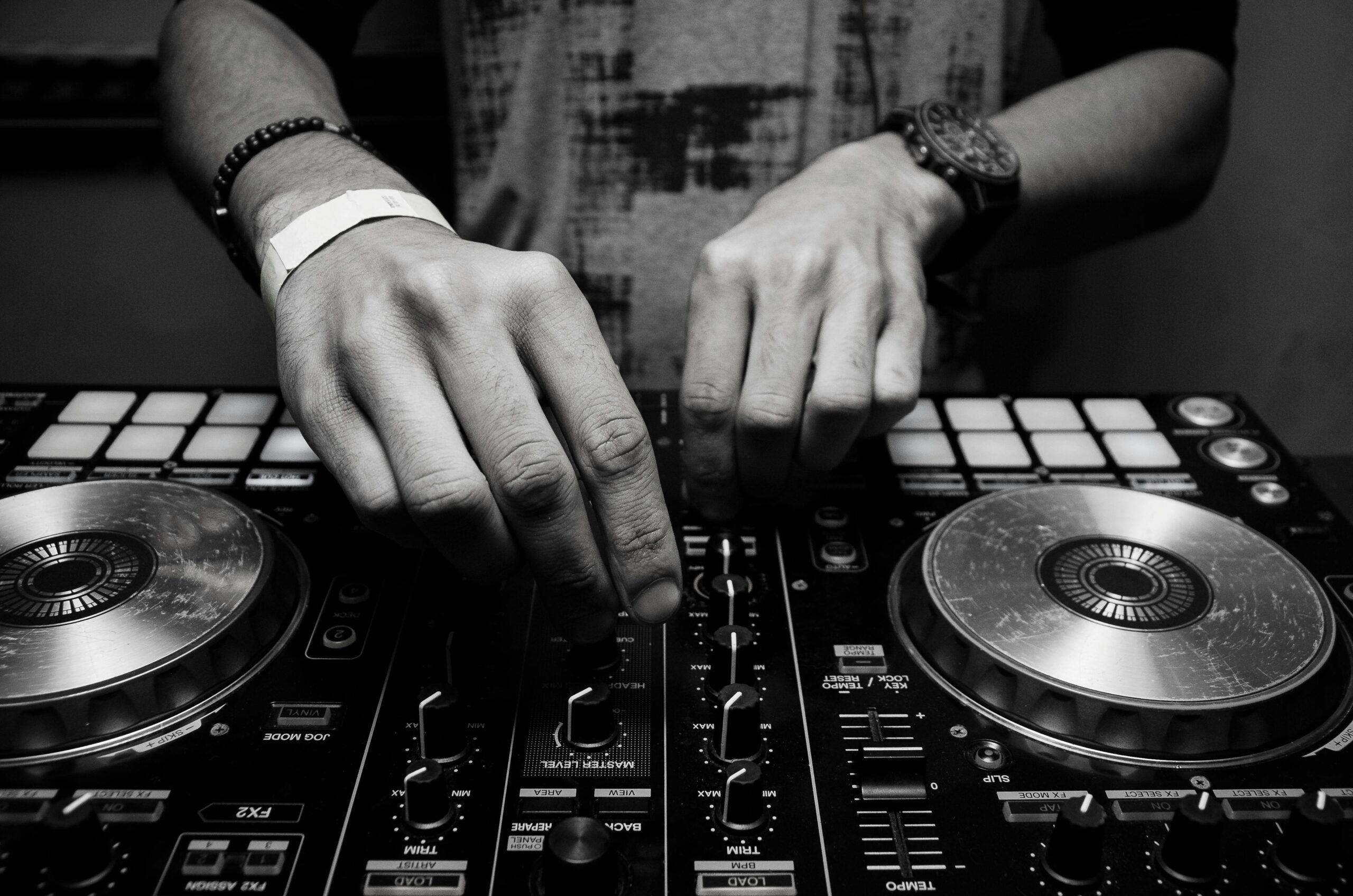 Close-up of a DJ's hands adjusting controls on a mixer in monochrome.